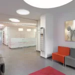 Modernes Wartezimmer mit grauen Stühlen, rotem Teppich und Glastrennwand in Zahnarztpraxis