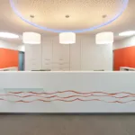 Weißer Empfangstresen in Zahnarztpraxis mit rotem Wellenmuster und moderner Beleuchtung