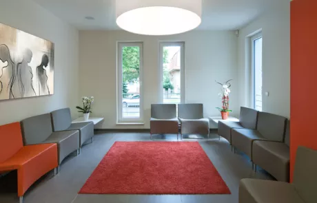 Wartezimmer mit grauen Stühlen und rotem Teppich