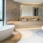 Modernes Badezimmer mit freistehender Badewanne, Doppelwaschtisch, großem Spiegel und Relaxsessel in elegantem, hellen Design.