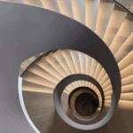 Moderne Wendeltreppe aus Holz mit integrierter Stufenbeleuchtung, fotografiert im spiralförmigen Blick nach unten.