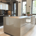 Moderne Designküche mit hochglänzender Kücheninsel, dunklen Einbauschränken, Holzfußboden und minimalistischer Pendelbeleuchtung.